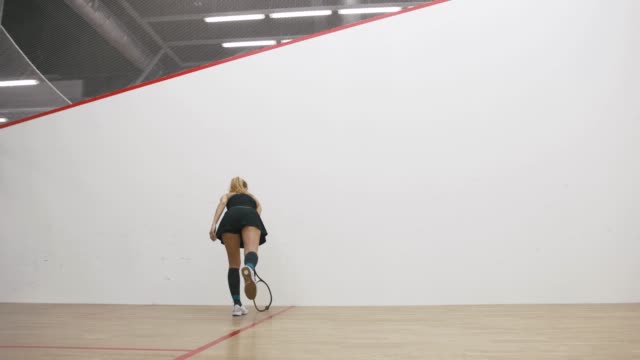 Young athletic man and woman play squash together in the squash court, slow motion, low angle view