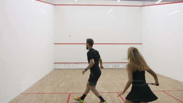 Young athletic man and woman play squash together in the squash court, slow motion