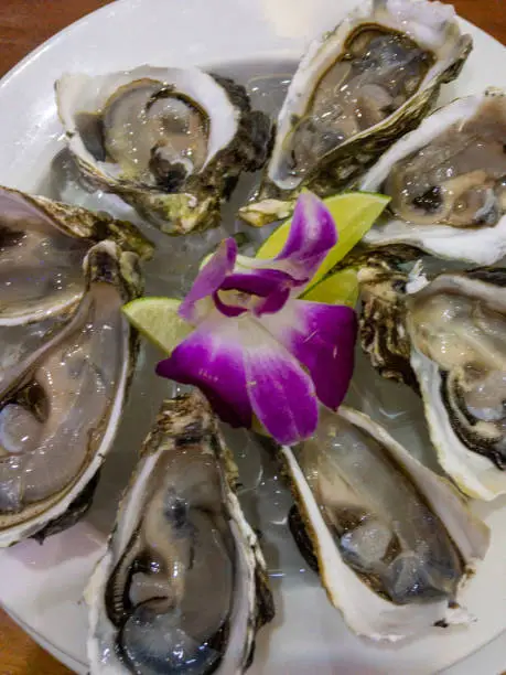 Photo of Fresh oysters with orchid flower and lemon top view, close up
