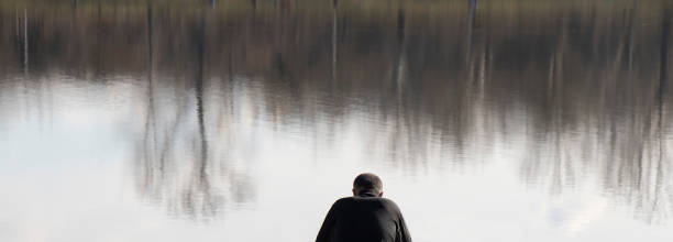 Belgrade, Serbia - February 2, 2020: One man in black sitting alone on a lake bank, with reflections on water