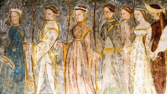 Alto Adige, Italy - October 11, 2019:  Close-up of a medieval Italian fresco, a group of people following a royal person with a crown, holding hands, painted in soft pastel colors.