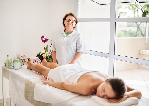 Shot of a senior massage therapist standing by a woman lying on table