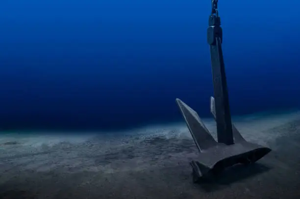 Photo of Ship anchor underwater on bottom in clean ocean water at anchorage. Marine shipping concept.