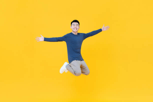 istock Young Asian man smiling and jumping with arms outstretched 1204923529