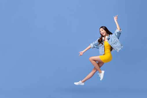 Young beautiful smiling Asian girl floating in mid-air with hand pointing up and down isolated on light blue background with copy space