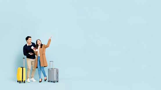 Lovely Asian couple tourists with baggage  about to go for winter honeymoon travel isolated on light blue background with copy space