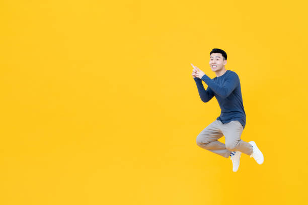 istock Asian man floating in mid-air pointing two fingers at empty space 1204923655