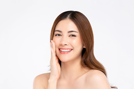 Beauty shot of smiling Asian woman model with clear fair skin doing hand touching face pose in white isolated background for skincare concept