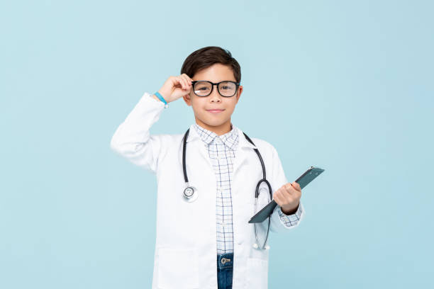 Smiling smart doctor boy with white medical coat and stethoscope Smiling smart doctor boy with white medical coat and stethoscope isolated on light blue background carnival costume stock pictures, royalty-free photos & images