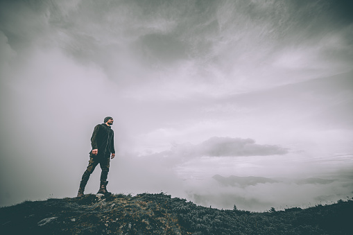 The man standing on the mountain on a beautiful clouds background