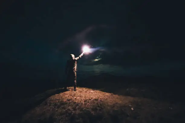 Photo of The male with a bright firework stick standing on the night mountain