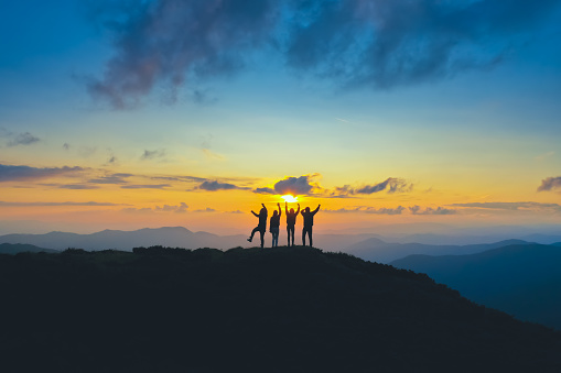 The four people standing on the beautiful mountain on the sunrise background