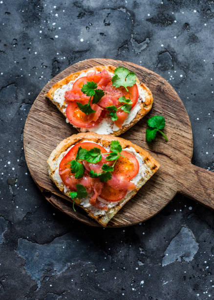 istock Smoked salmon, tomatoes, cream cheese, cilantro sandwich on a rustic cutting board on a dark background, top view 1204949571