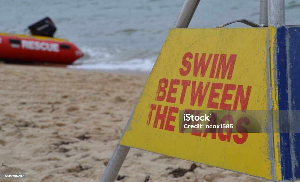 Notice on the beach to swim between the flags in Australia Warning sign to swimmers with inflatable rescue boat in the background Flag Stock Photo