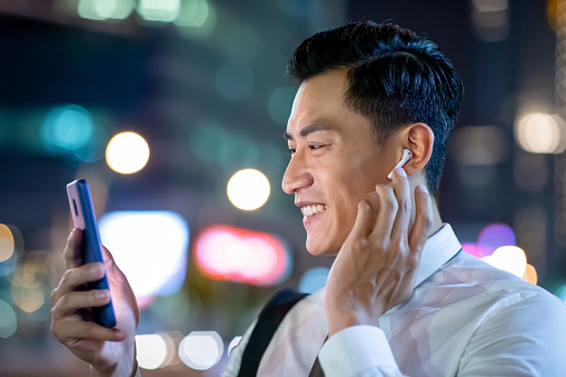 close up of asian man speak to phone by wearing wireless earbuds while walking on the street