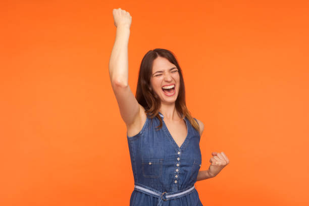 hooray, sieg! glücklich überglücklich begeisterte brünette frau in denim kleid tanzen schreien aus aufregung - super powers stock-fotos und bilder