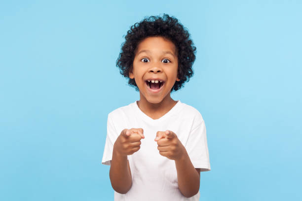 Hey you! Portrait of happy little boy with curly hair pointing finger to camera and laughing loudly with surprised face Hey you! Portrait of happy little boy with curly hair pointing finger to camera and laughing loudly with surprised face, teasing making fun of you. indoor studio shot isolated on blue background signing photos stock pictures, royalty-free photos & images