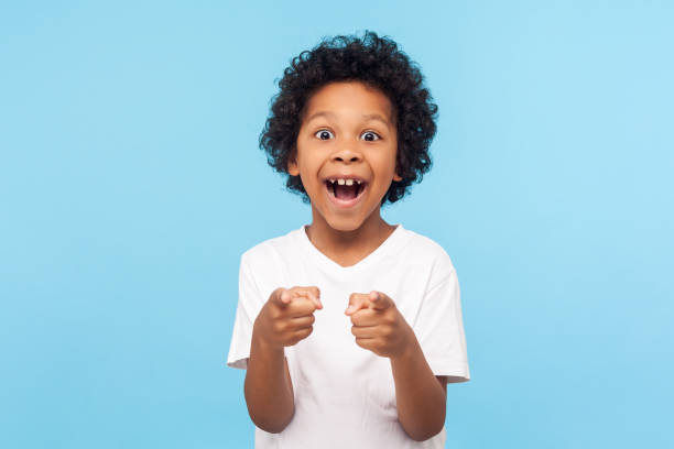 ei, você! retrato de menino feliz com cabelo encaracolado apontando dedo para câmera e rindo alto com rosto surpreso - child excitement awe fun - fotografias e filmes do acervo