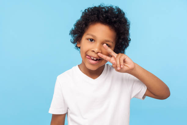 tシャツの巻き毛を持つ陽気な気ままな小さな男の子の肖像画は、鼻を摘み取り、幸せな顔で舌を突き出す - african descent addiction african ethnicity rudeness ストックフォトと画像