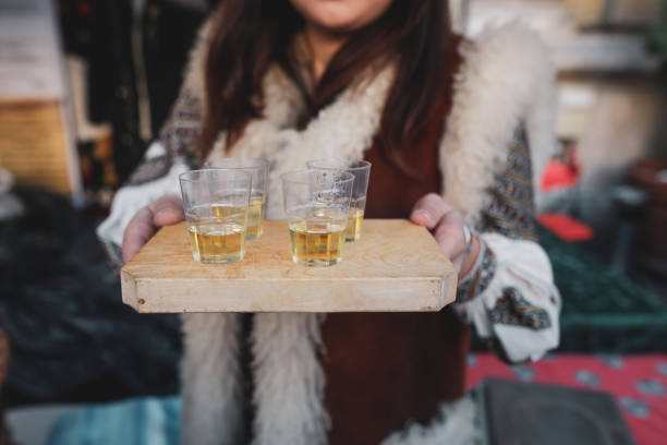 shallow depth of field (selective focus) image with a woman holding a wooden plate with palinca (or tuica), romanian traditional plum brandy. - slivovitz imagens e fotografias de stock