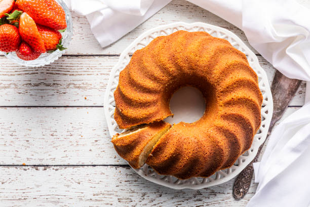 une table en bois blanc avec un gâteau de bundt, kugelhupf ou sockerkaka et un bol de fraises - quatre quarts photos et images de collection