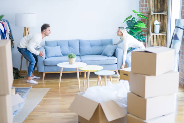 istock Young beautiful couple moving sofa at new home around cardboard boxes 1204994483