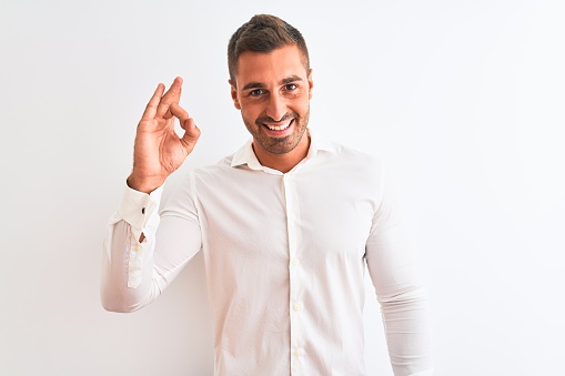 Young handsome business man wearing elegant shirt over isolated background smiling positive doing ok sign with hand and fingers. Successful expression.