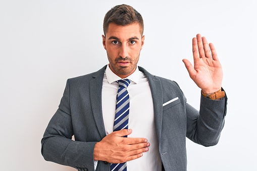 Young handsome business man wearing suit and tie over isolated background Swearing with hand on chest and open palm, making a loyalty promise oath