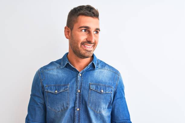 istock Young handsome man wearing denim jacket standing over isolated background looking away to side with smile on face, natural expression. Laughing confident. 1204996450