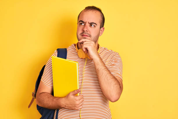 istock Student man wearing backpack headphones holding notebook over isolated yellow background serious face thinking about question, very confused idea 1204997733