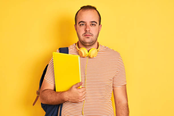 istock Student man wearing backpack headphones holding notebook over isolated yellow background with a confident expression on smart face thinking serious 1204997764