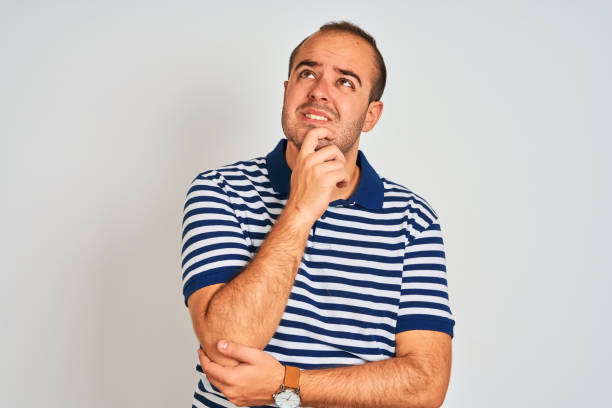 istock Young man wearing casual striped polo standing over isolated white background Thinking worried about a question, concerned and nervous with hand on chin 1204998877