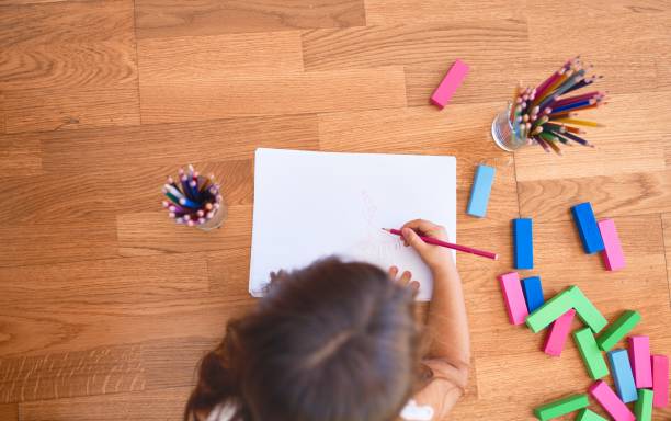 istock Adorable toddler lying down on the floor drawing using paper and pencils at kindergarten 1205000574