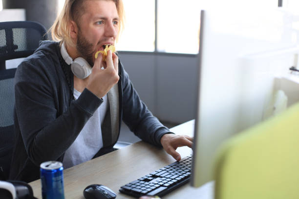 istock Concentrated young man in casual clothing using computer, streaming playthrough or walkthrough video and eating chips. 1205000706