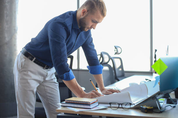 istock Technology and planning. Shot of a young designer at work with some blueprints and a laptop. 1205001137
