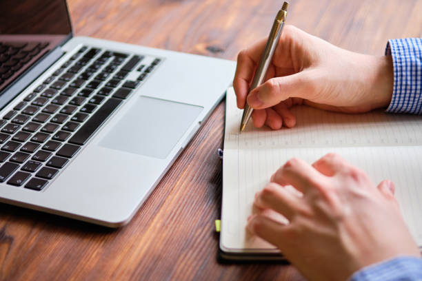 istock A man makes notes in a diary next to a laptop on a wooden table. 1205001766