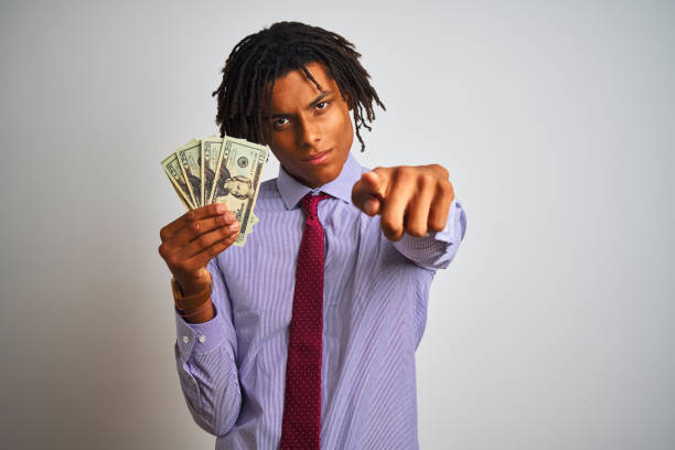istock Afro american businessman with dreadlocks holding dollars over isolated white background pointing with finger to the camera and to you, hand sign, positive and confident gesture from the front 1205002040