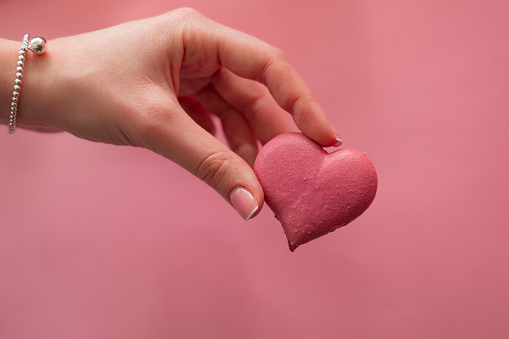 Female hand holding pink macaroon in the heart shape