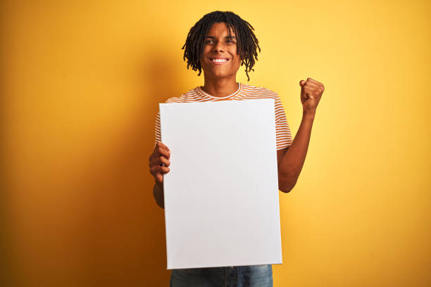 istock Afro american man with dreadlocks holding banner over isolated yellow background screaming proud and celebrating victory and success very excited, cheering emotion 1205003824