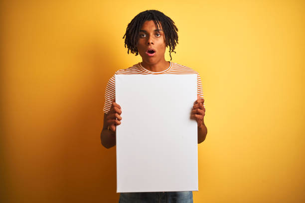 istock Afro american man with dreadlocks holding banner over isolated yellow background scared in shock with a surprise face, afraid and excited with fear expression 1205004082