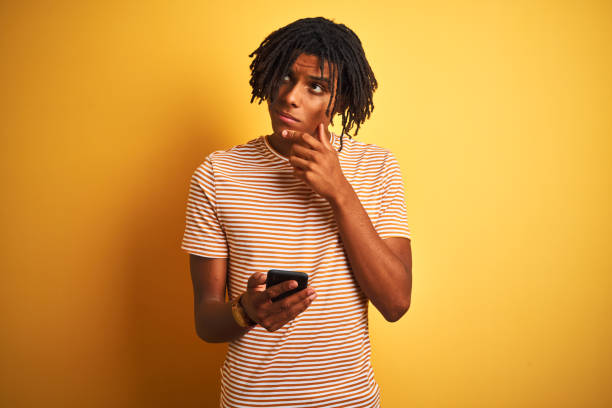 istock Afro american man with dreadlocks using smartphone over isolated yellow background serious face thinking about question, very confused idea 1205004260