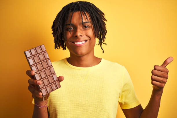 istock Afro american man with dreadlocks eating chocolate bar over isolated yellow background happy with big smile doing ok sign, thumb up with fingers, excellent sign 1205005134