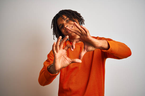 istock Afro american man with dreadlocks wearing orange sweater over isolated white background smiling in love showing heart symbol and shape with hands. Romantic concept. 1205005415