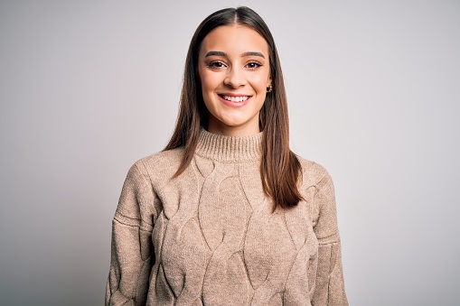 Young beautiful brunette woman wearing casual sweater standing over white background with a happy and cool smile on face. Lucky person.