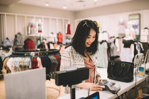 an asian chinese beautiful woman with sunglasses is paying for her clothes at the retail counter in a boutique shop