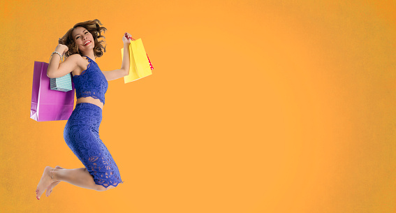 Asian woman holding fancy shopping bags jumping on an orange background