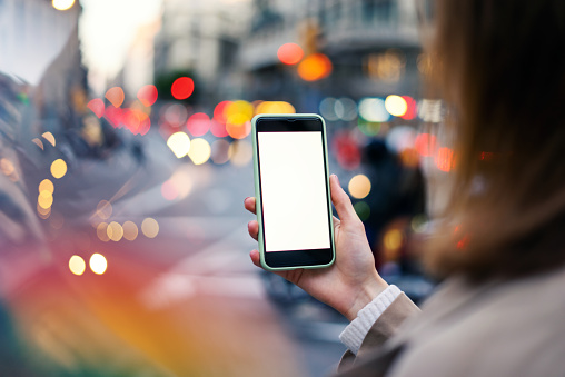 Closeup image of female hands holding modern smartphone with blank screen. Mockup ready for text message or content. Woman's hands with cellphone. Empty display. Night street, bokeh light