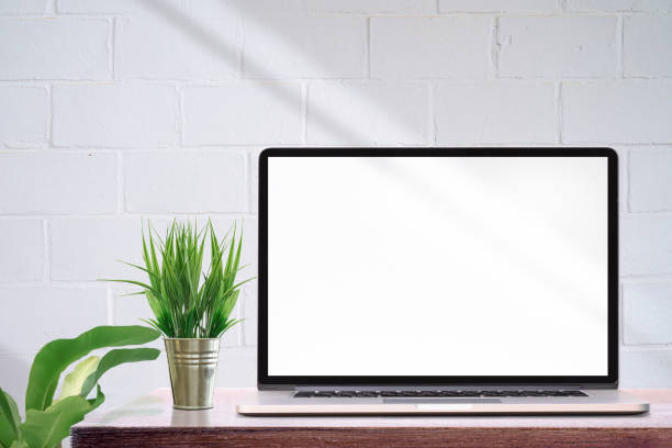 istock Mockup laptop computer with blank screen and houseplant on wooden table, white brick wall and copy space. 1205011224