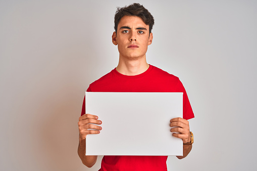 Teenager boy holding advertising banner with blank space over isolated background with a confident expression on smart face thinking serious