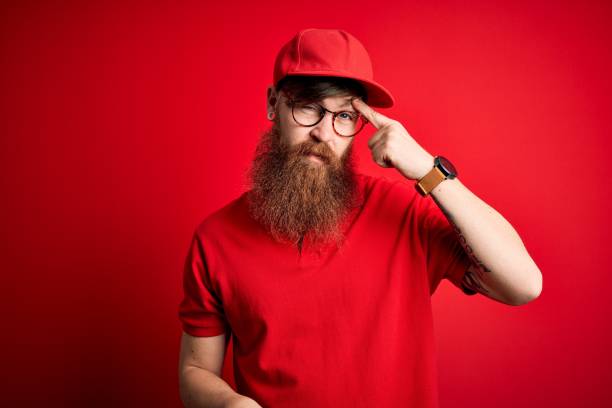 istock Young handsome delivery man wearing glasses and red cap over isolated background pointing unhappy to pimple on forehead, ugly infection of blackhead. Acne and skin problem 1205015851